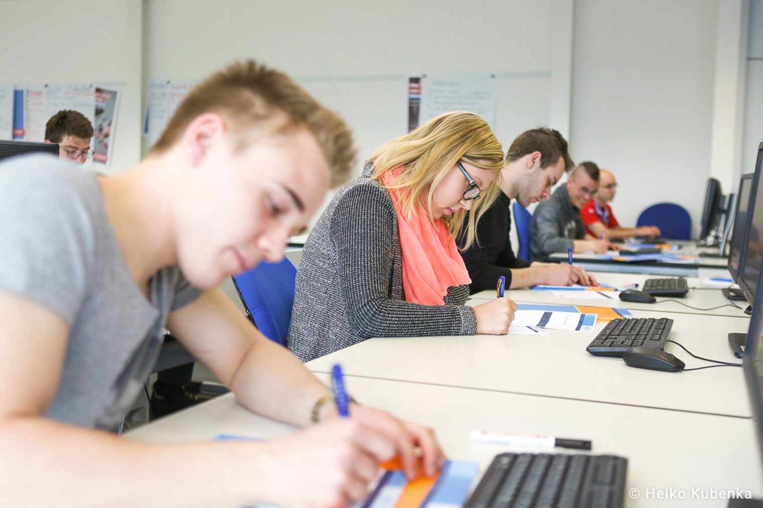 Teilnehmende eines Seminar schreiben auf Arbeitsblätter Auszubildende nehmen an einem Seminar teil und schreiben auf Arbeitsblätter, während sie vor Computern sitzen.