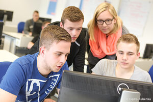 Auszubildende befinden sich in einem Seminarraum und schauen gemeinsam auf einen Monitor.