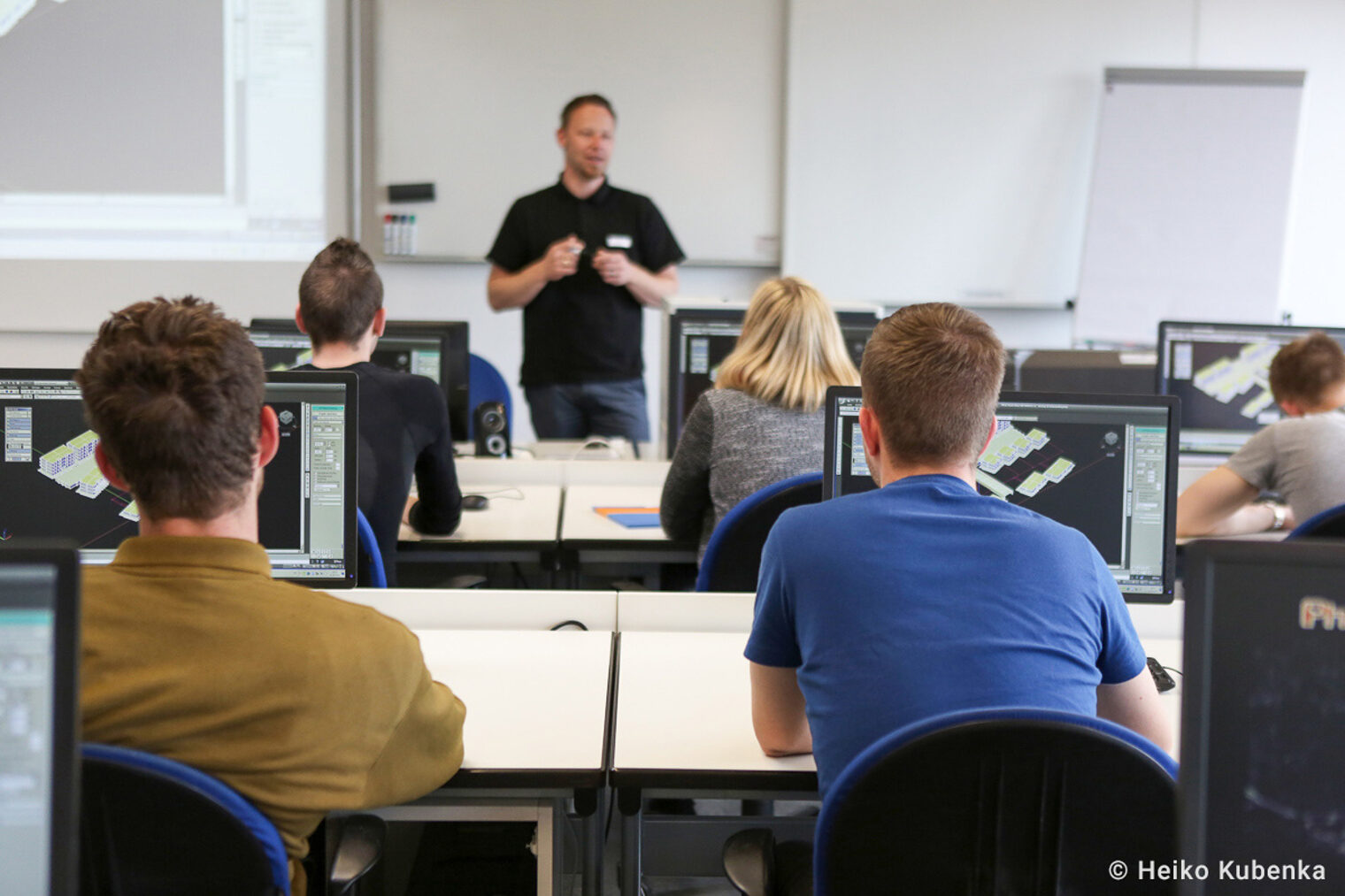 Eine Lehrkraft unterrichtet Auszubildende Eine Lehrkaft steht vorne in einem Seminarraum und unterrichtet Auszubildende, die am PC arbeiten