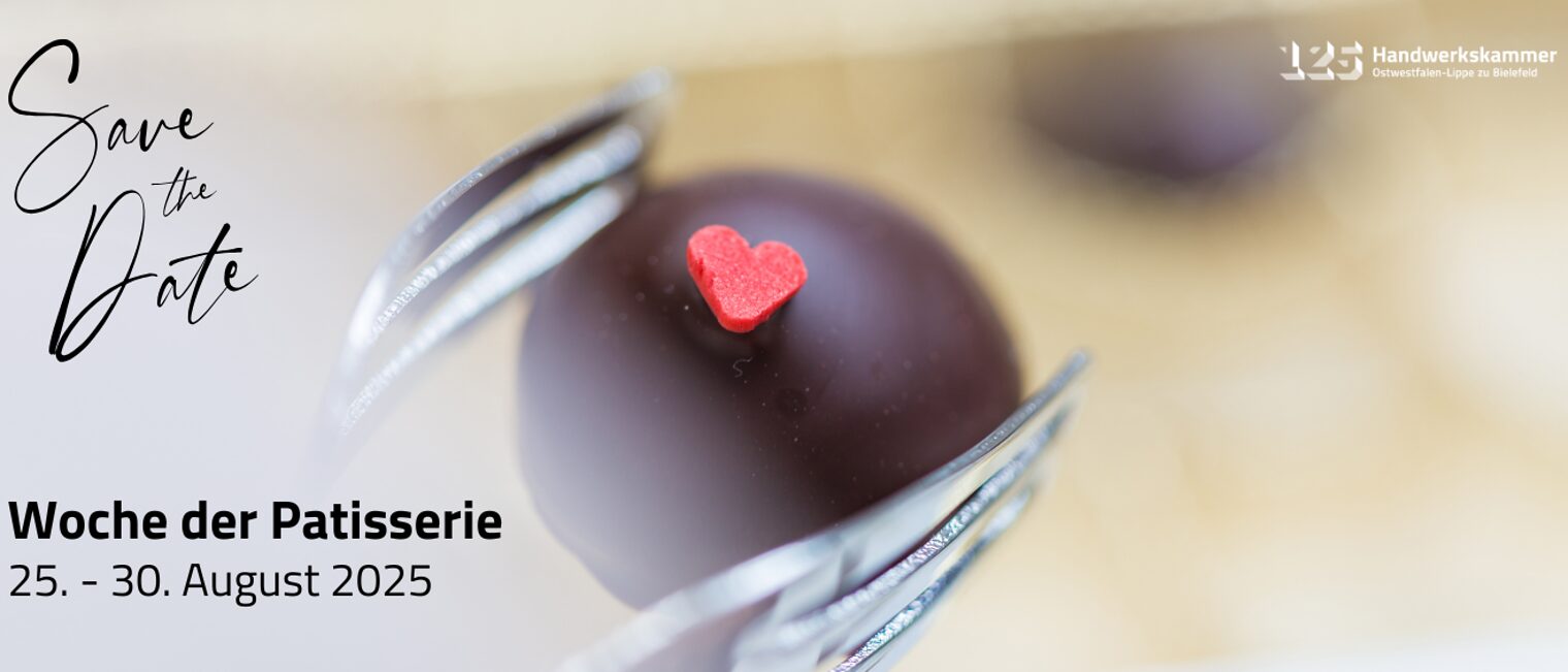 Wochen der Patisserie Eine Schokoladenpraline mit einem roten Herz wird mit einer Pralinengabel gehalten.